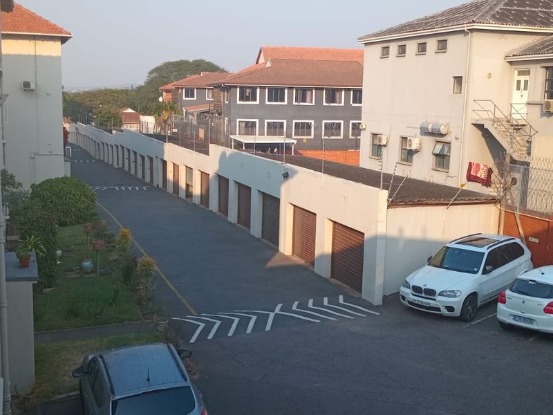 An elevated view of the apartment complex rear area, featuring a paved driveway, row of garages, and security fencing.
