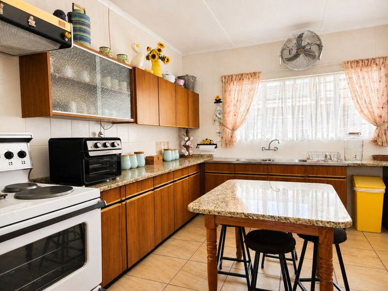 A functional kitchen featuring wooden cabinetry, granite countertops, tiled flooring, and a stainless steel sink, offering a classic and practical layout.