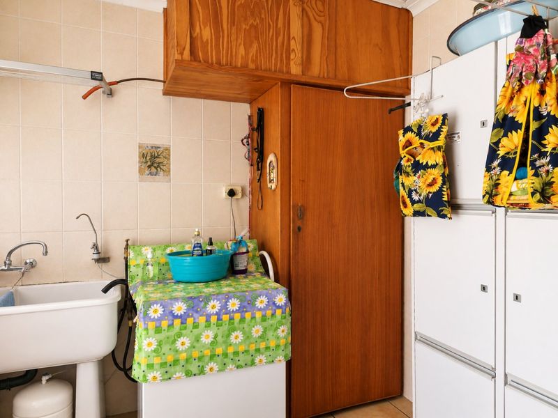 A functional laundry room featuring a utility sink, tiled walls, and built-in wooden storage cabinetry.