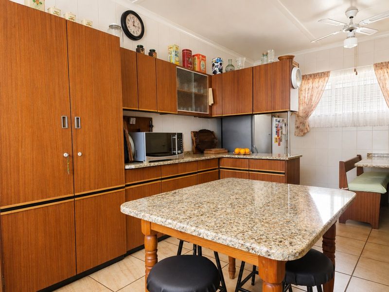 A functional kitchen featuring wood-look laminate cabinetry, granite countertops, tiled flooring, and a ceiling fan, offering a classic, dated aesthetic.