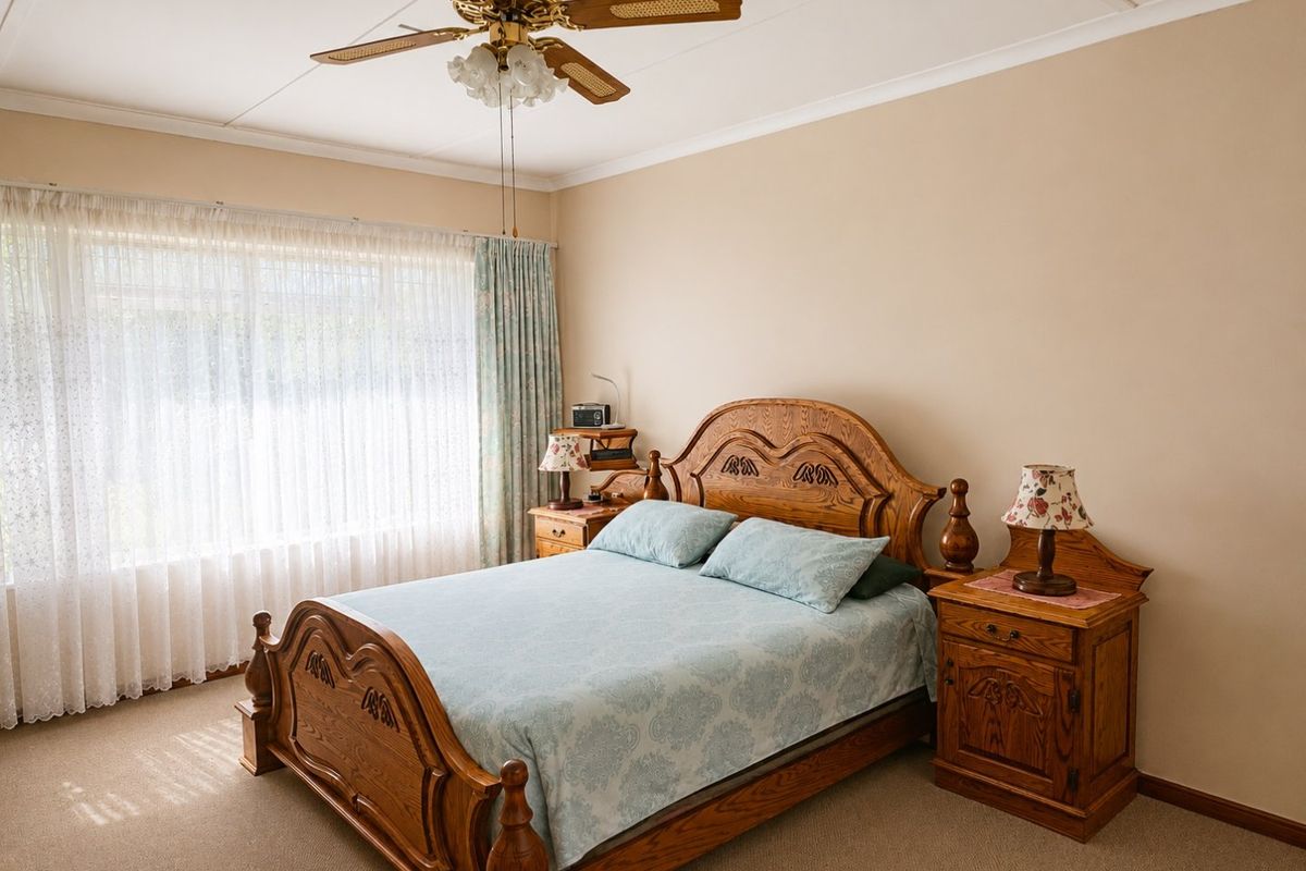 A well-maintained bedroom featuring neutral wall tones, carpeted flooring, and a classic ceiling fan, offering a comfortable and functional living space.