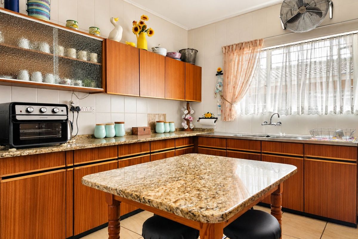 A functional kitchen featuring warm-toned wooden cabinetry, granite countertops, a double basin sink, and tiled finishes throughout.