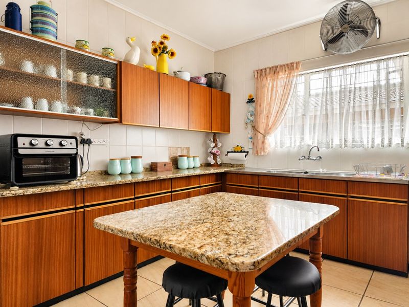 A functional kitchen featuring warm-toned wooden cabinetry, granite countertops, a double basin sink, and tiled finishes throughout.