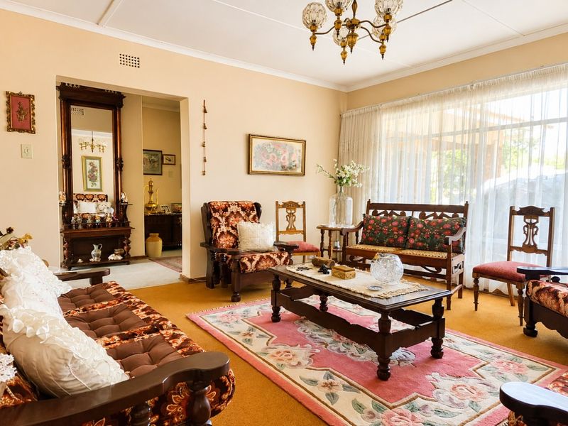A traditional living room featuring carpeted flooring, a classic chandelier, and large windows allowing for natural light.