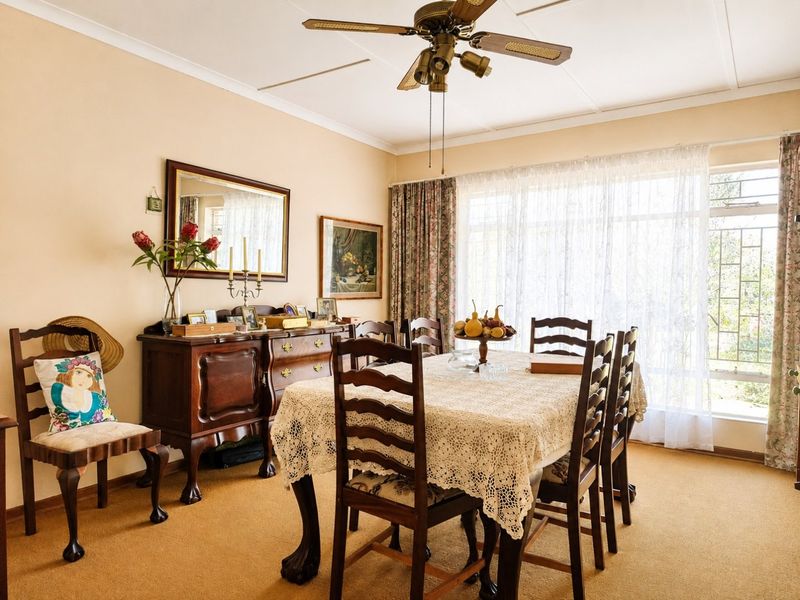A traditional dining room featuring a ceiling fan, carpeted flooring, and large windows allowing for natural light.