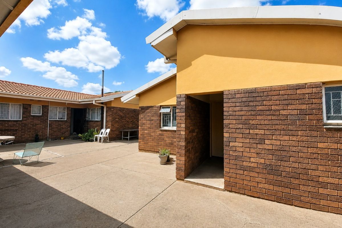 A spacious rear courtyard featuring face brick walls, concrete paving, and access to the main dwelling structure.