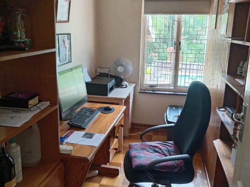 A compact home office featuring parquet flooring, built-in timber shelving, and wood-paneled walls with a window overlooking the exterior.