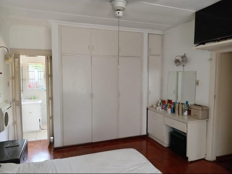 Bedroom featuring built-in cupboards, a vanity unit, ceiling fan, and hardwood flooring, with direct access to an en-suite bathroom.