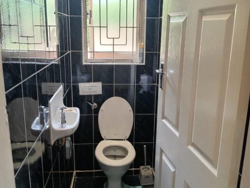 A compact guest bathroom featuring dark tiled walls and flooring, a wall-mounted basin, and a standard toilet with security bars on the window.