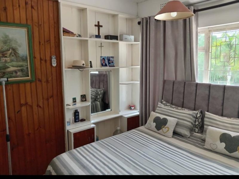 A bedroom featuring timber wall paneling, a built-in white shelving unit, and a window fitted with security bars.