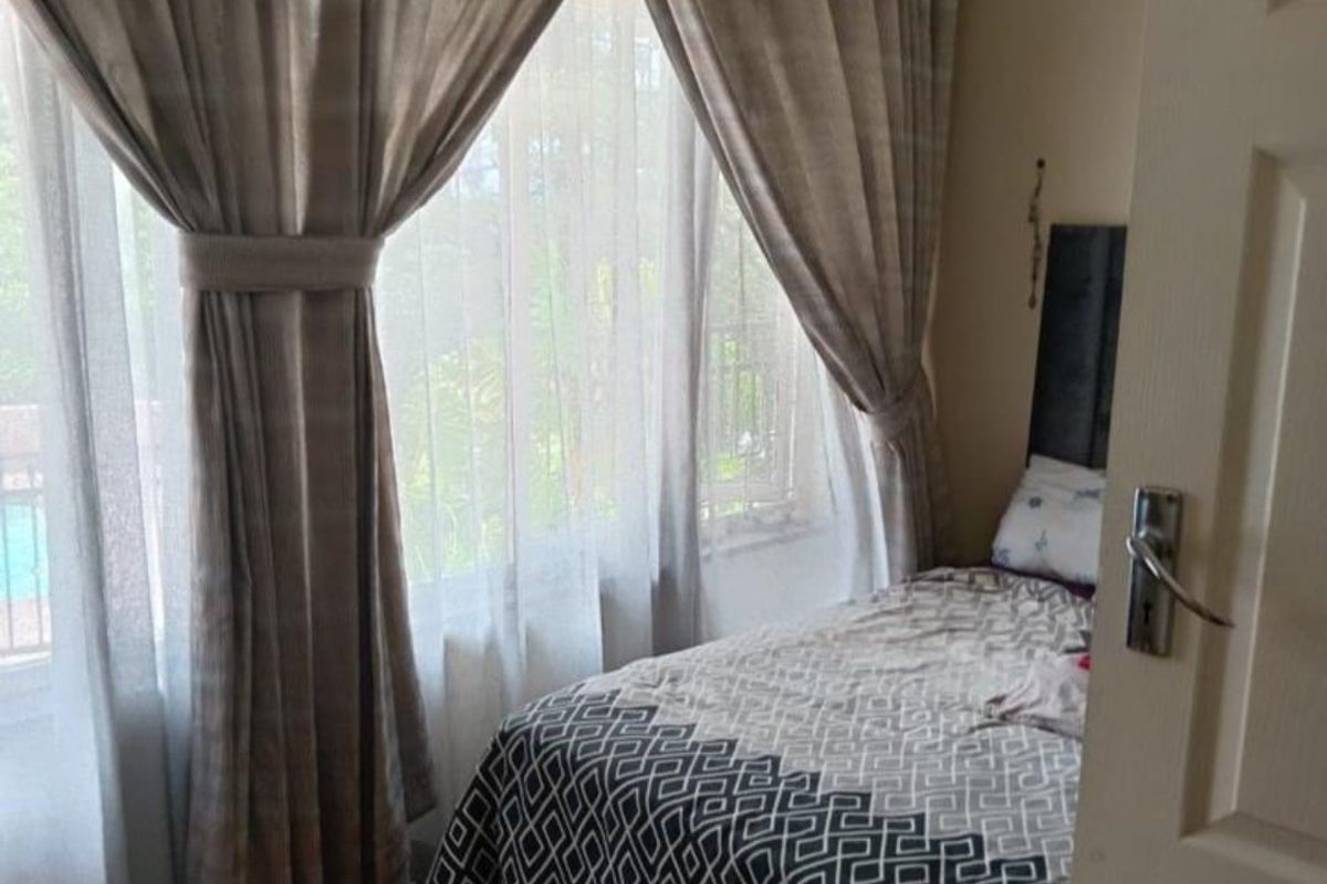 A cozy bedroom featuring warm parquet flooring, neutral wall tones, and large windows that allow for natural light.