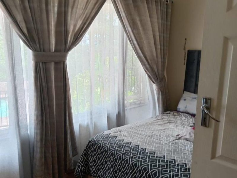 A cozy bedroom featuring warm parquet flooring, neutral wall tones, and large windows that allow for natural light.