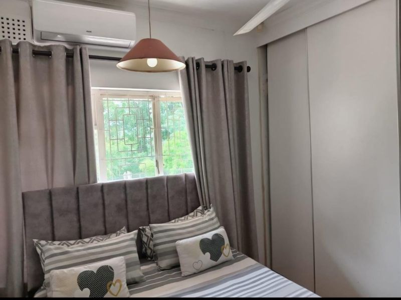A bedroom featuring a built-in wardrobe, split-system air conditioning unit, and a window fitted with security bars.
