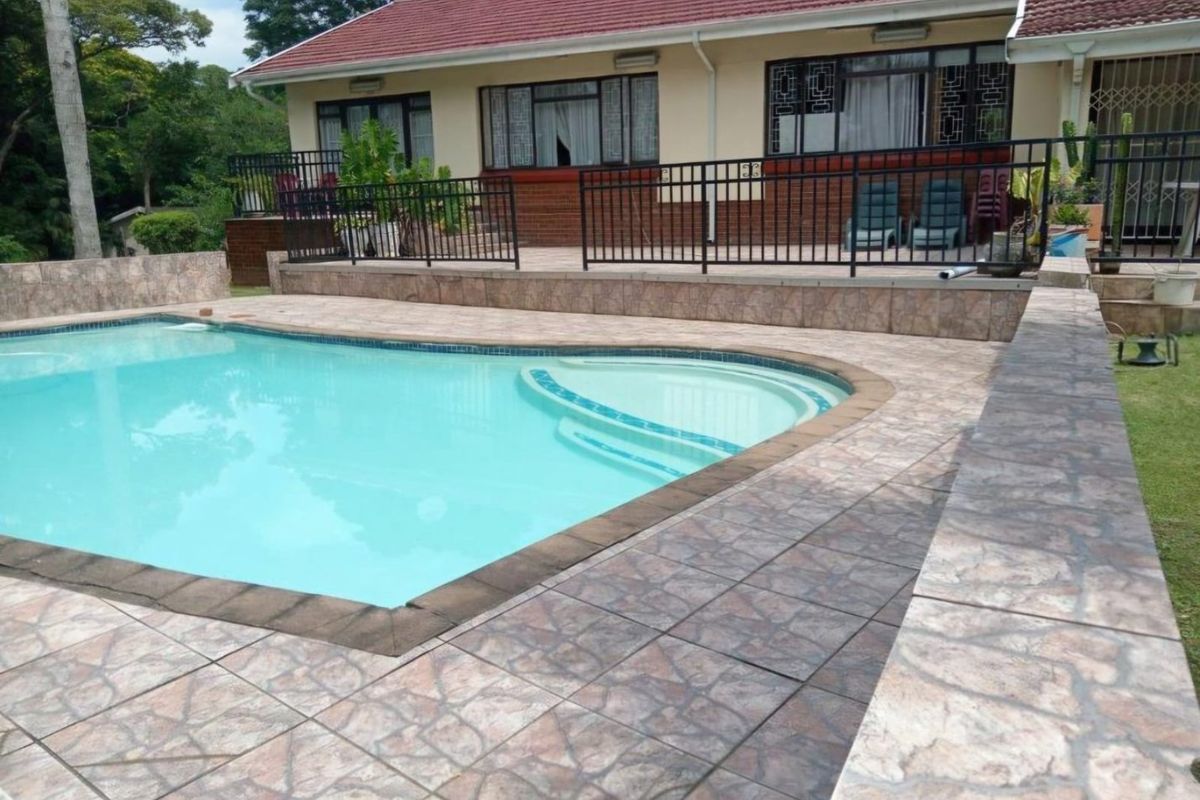 Outdoor pool area featuring a tiled deck, metal safety railing, and direct access to the rear patio of the house.