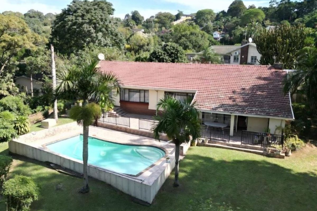 Aerial view of a residential property featuring a swimming pool, tiled roof, and a spacious garden area.