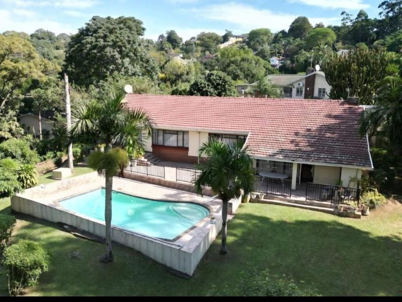 Aerial view of a residential property featuring a swimming pool, tiled roof, and a spacious garden area.