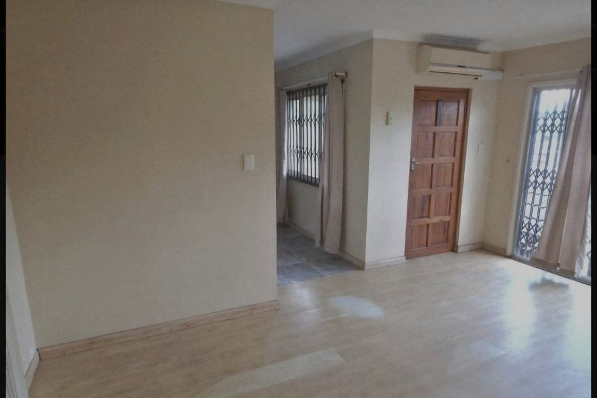 An empty living room featuring laminate flooring, a split-system air conditioner, and access to an adjacent area through a timber door.