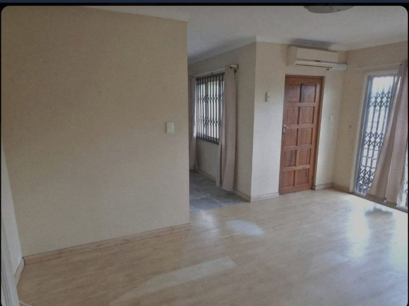 An empty living room featuring laminate flooring, a split-system air conditioner, and access to an adjacent area through a timber door.