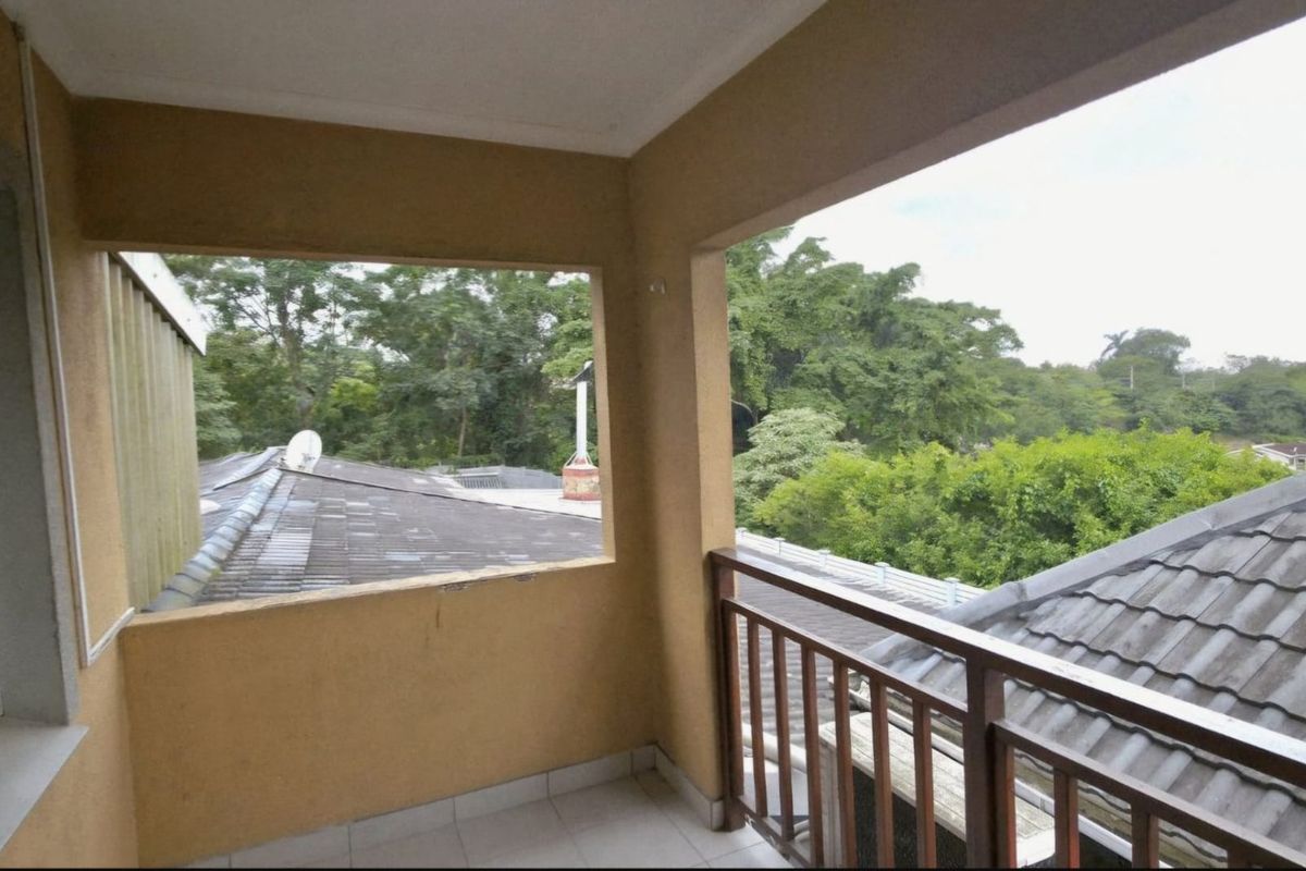 A covered balcony featuring tiled flooring and a timber balustrade, offering an elevated view of the surrounding trees and neighboring rooftops.