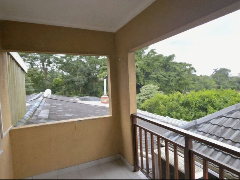 A covered balcony featuring tiled flooring and a timber balustrade, offering an elevated view of the surrounding trees and neighboring rooftops.
