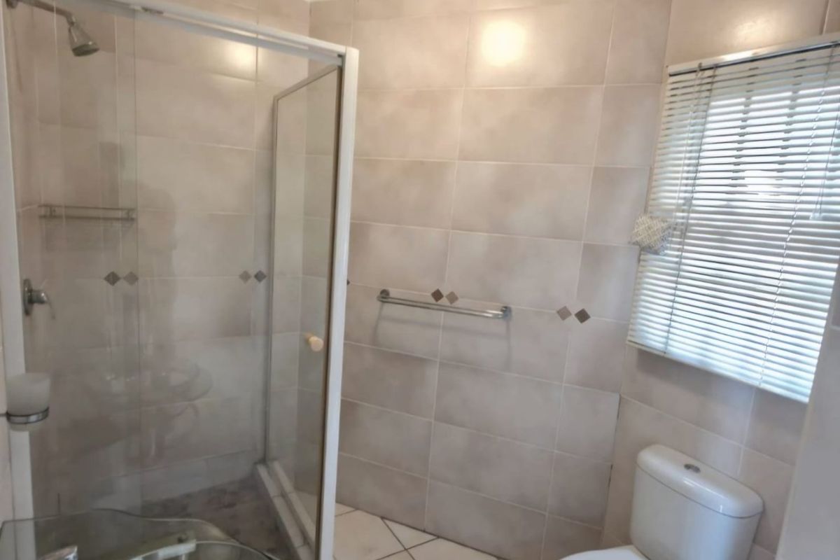 A functional bathroom featuring a glass shower enclosure, tiled walls and flooring, and a standard toilet.