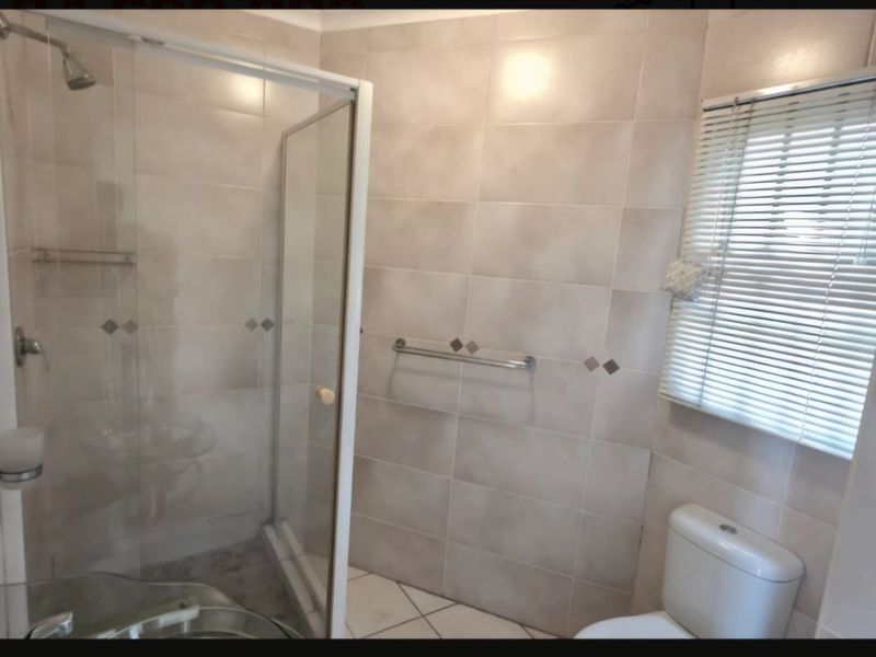 A functional bathroom featuring a glass shower enclosure, tiled walls and flooring, and a standard toilet.