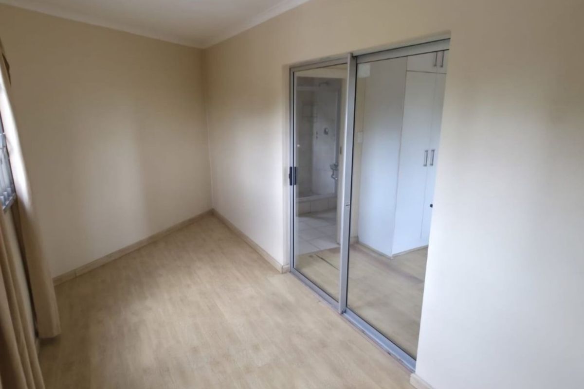 A bright, empty bedroom featuring laminate flooring, built-in cupboards, and a sliding glass door providing access to an en-suite bathroom.