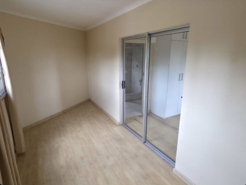 A bright, empty bedroom featuring laminate flooring, built-in cupboards, and a sliding glass door providing access to an en-suite bathroom.