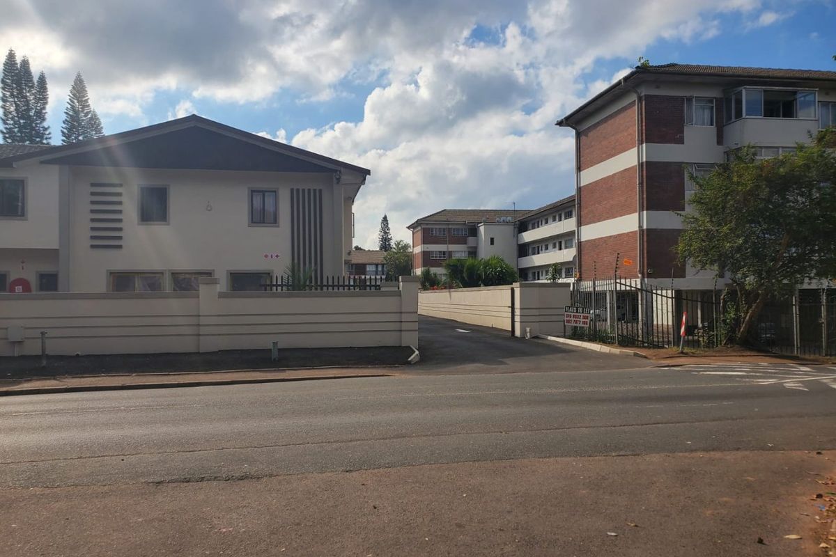 Street view of a commercial property complex featuring brick and plastered facades, secure perimeter walling with electric fencing, and an asphalt driveway entrance.