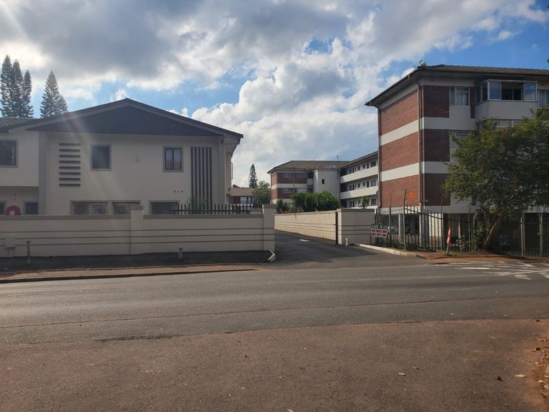 Street view of a commercial property complex featuring brick and plastered facades, secure perimeter walling with electric fencing, and an asphalt driveway entrance.