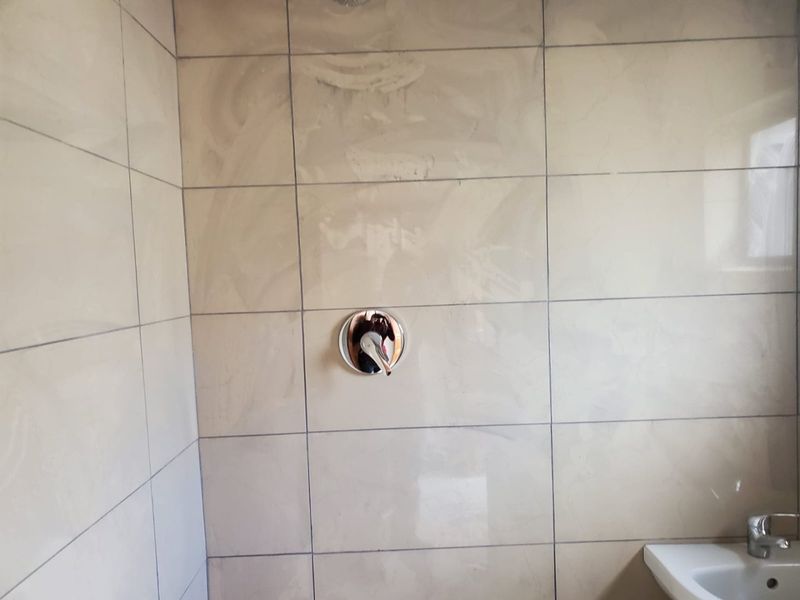 A bathroom shower area featuring neutral ceramic wall tiles, a chrome shower mixer, and a basin mixer.