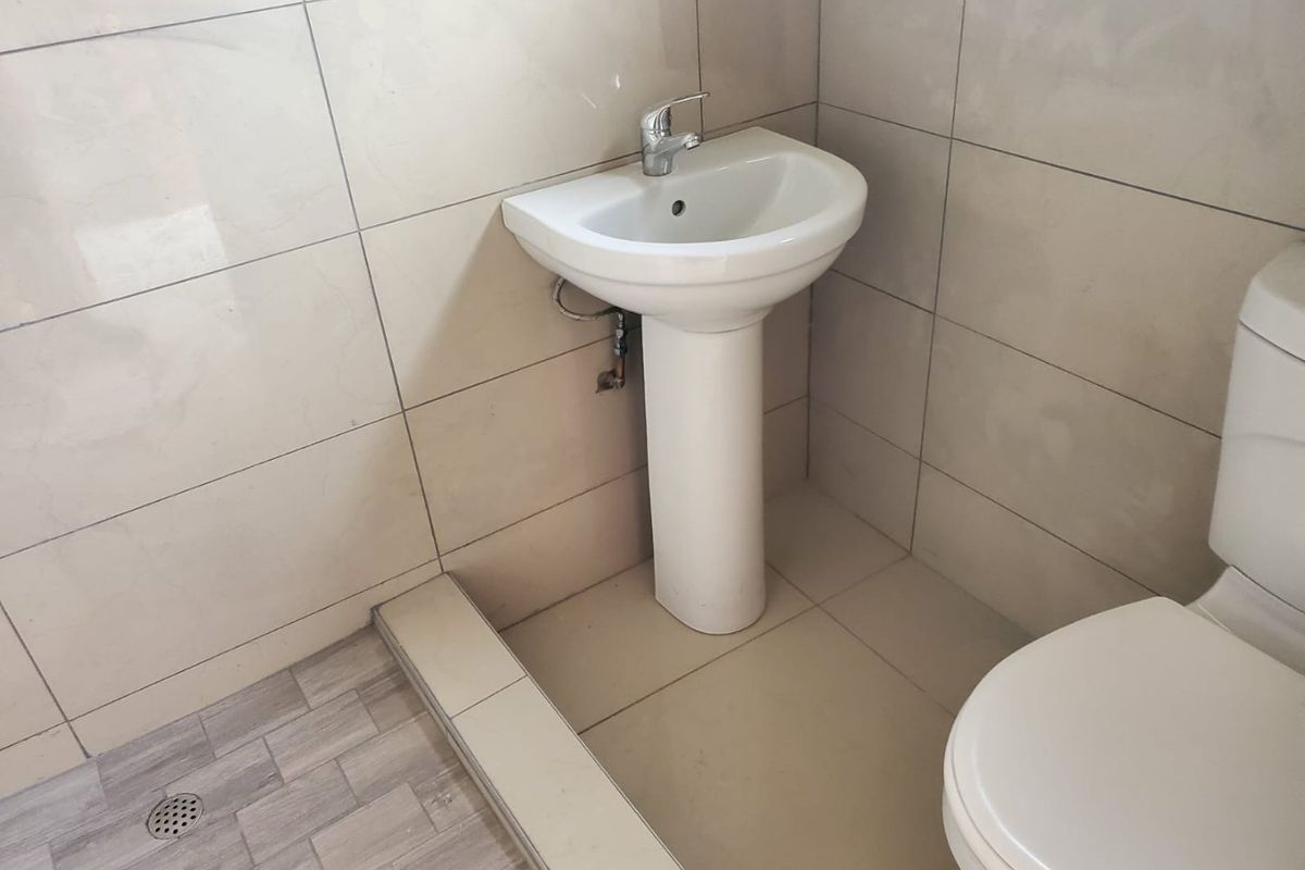 A functional bathroom featuring a pedestal basin with chrome mixer tap, tiled walls and flooring, and a standard toilet.