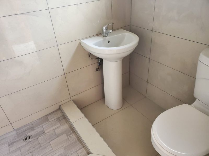 A functional bathroom featuring a pedestal basin with chrome mixer tap, tiled walls and flooring, and a standard toilet.