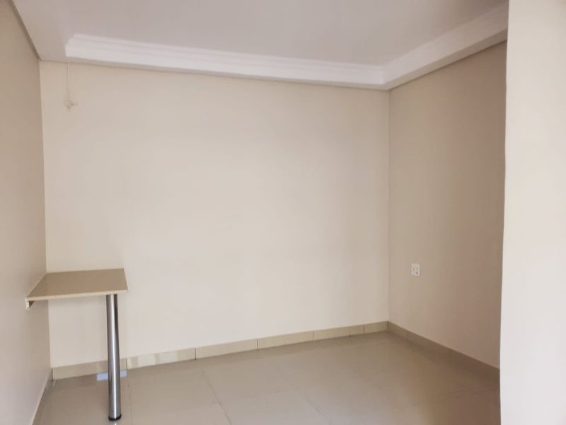 A clean, empty office space featuring neutral walls, tiled flooring, cove cornicing, and a built-in desk surface.