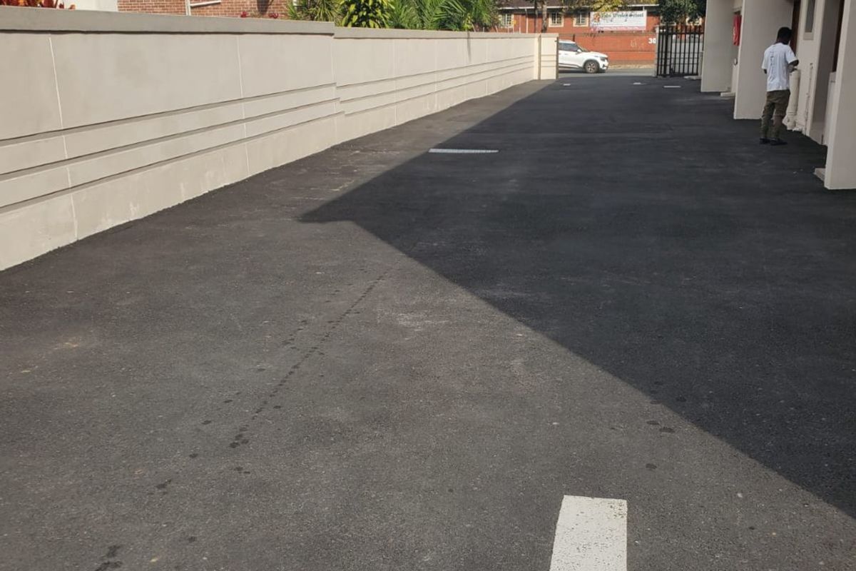 A paved driveway area alongside a commercial building, featuring a boundary wall and clear directional markings on the asphalt surface.