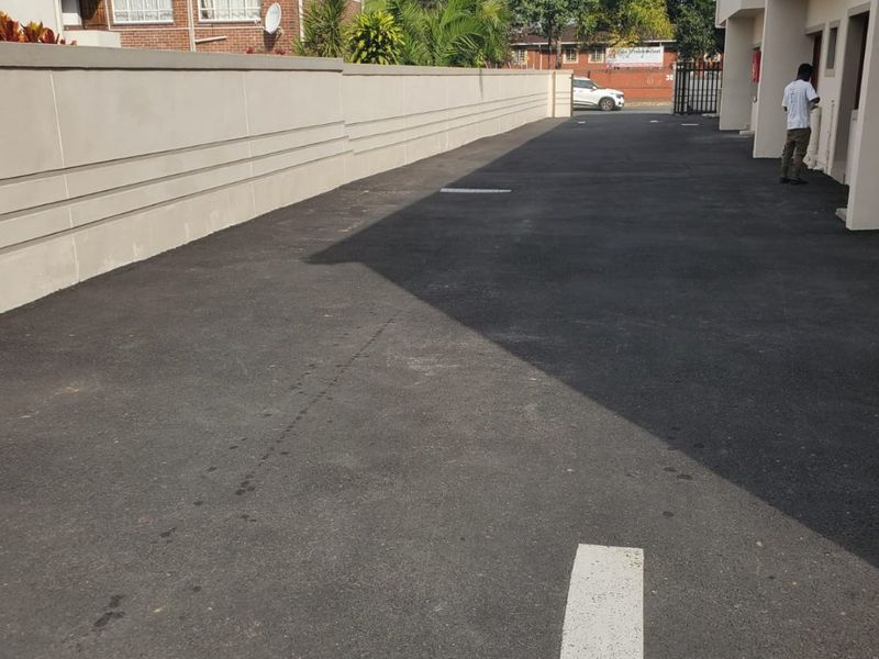 A paved driveway area alongside a commercial building, featuring a boundary wall and clear directional markings on the asphalt surface.