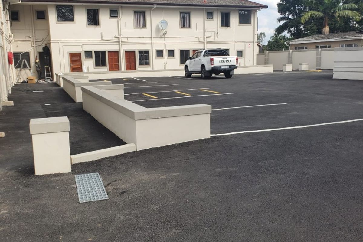 A well-maintained commercial exterior rear area featuring a paved parking lot, retaining walls, and access to multiple building units.
