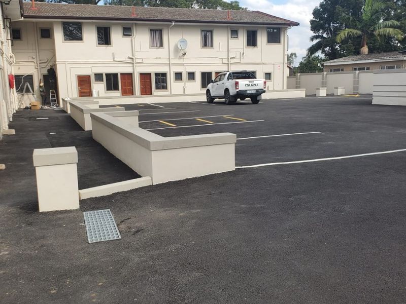 A well-maintained commercial exterior rear area featuring a paved parking lot, retaining walls, and access to multiple building units.