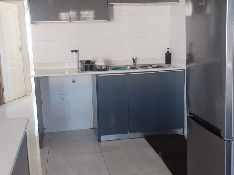 A functional kitchen featuring modern grey cabinetry, stone countertops, a tiled backsplash, and tiled flooring, providing a clean and practical workspace.