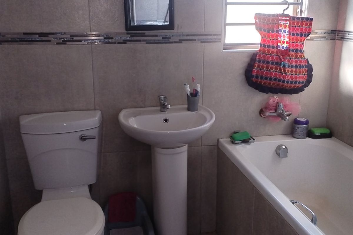 A functional bathroom featuring a pedestal basin, toilet, and bathtub with neutral wall tiling and decorative mosaic accents.