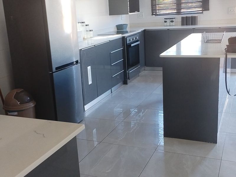 Modern kitchen featuring dark cabinetry, a central island with stone countertops, built-in oven, hob, and polished tiled flooring.