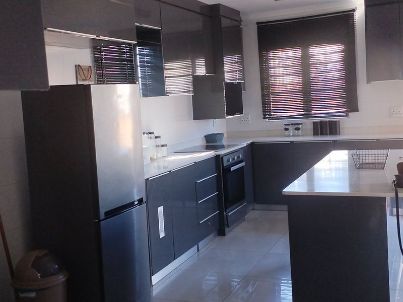 Modern kitchen featuring dark grey cabinetry, stone countertops, a central island, and built-in appliances with tiled flooring and natural light.