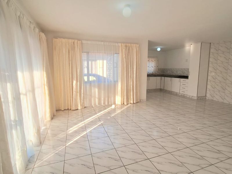 Spacious open-plan living and kitchen area featuring neutral tiled flooring and clean, functional built-in cabinetry.
