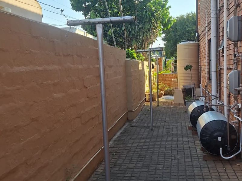 A side exterior area featuring a paved walkway, brick boundary wall, external electric geysers, and a fixed washing line.