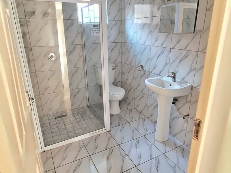 A clean, modern bathroom featuring marble-look wall and floor tiles, a glass shower enclosure, a pedestal basin, and a wall-mounted medicine cabinet.
