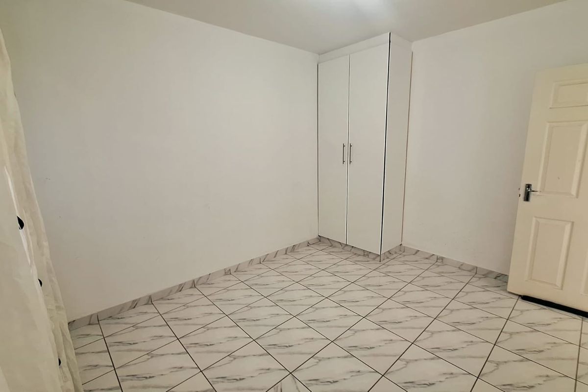 A clean, empty bedroom featuring white walls, marble-effect tiled flooring, and a built-in wardrobe.