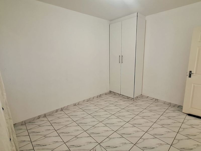 A clean, empty bedroom featuring white walls, marble-effect tiled flooring, and a built-in wardrobe.