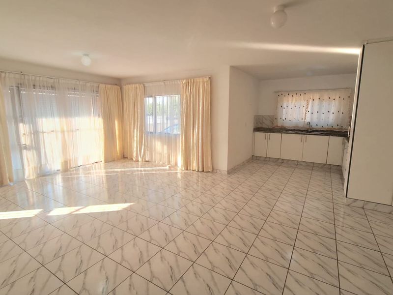 Spacious open-plan living and kitchen area featuring uniform marble-look tiled flooring, neutral walls, and built-in kitchen cabinetry.