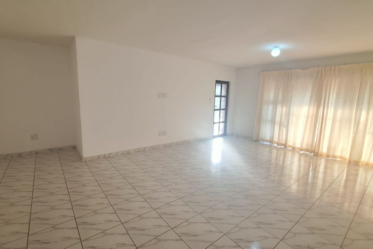 A spacious, empty living area featuring neutral tiled flooring, ample natural light from large glass doors, and a clean, blank canvas for interior design.