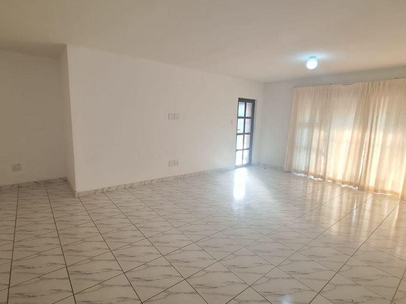 A spacious, empty living area featuring neutral tiled flooring, ample natural light from large glass doors, and a clean, blank canvas for interior design.